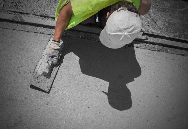 Worker smoothing and repairing a concrete surface with a hand trowel